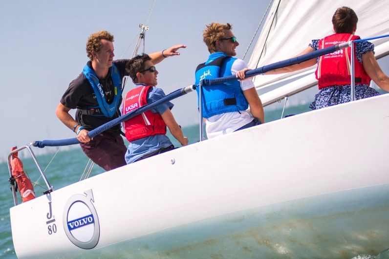 A UKSA trained instructor on a yacht giving advice to trainee sailors.