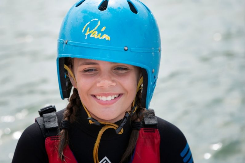 A school child smiling whilst wearing a wetsuit and helmet